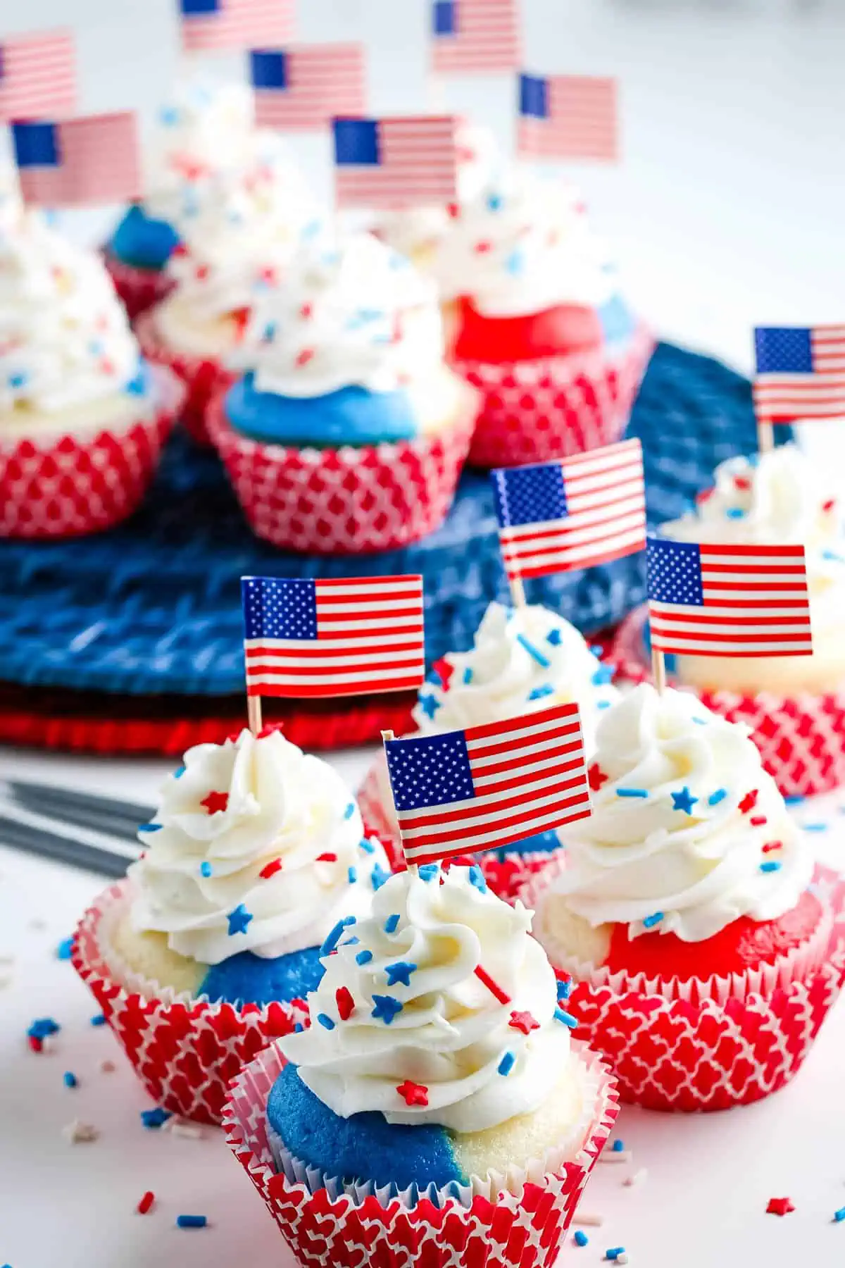 red white and blue cupcakes decorated as July 4th cupcakes with buttercream frosting, sprinkles, and American flag toppers