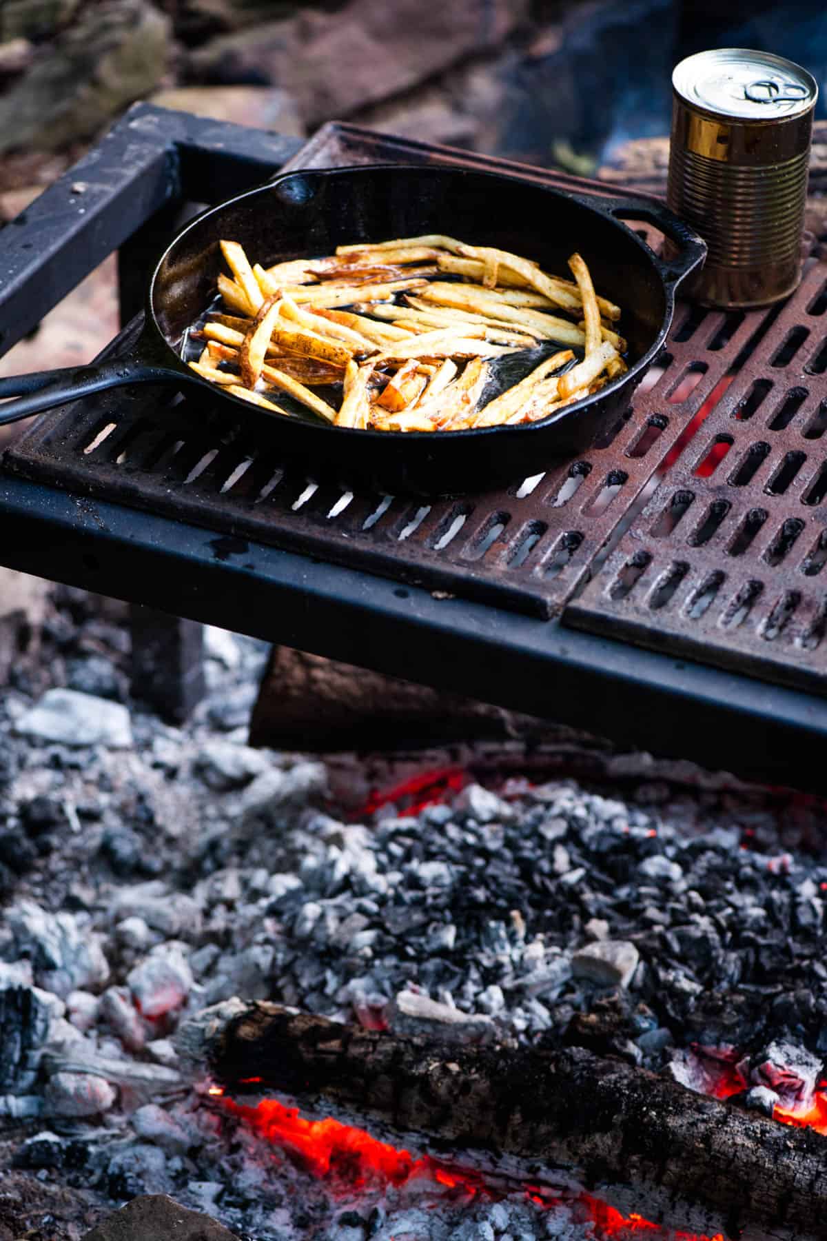 crispy French fries cooking in a cast iron skillet on a campfire grill over a bed of hot coals