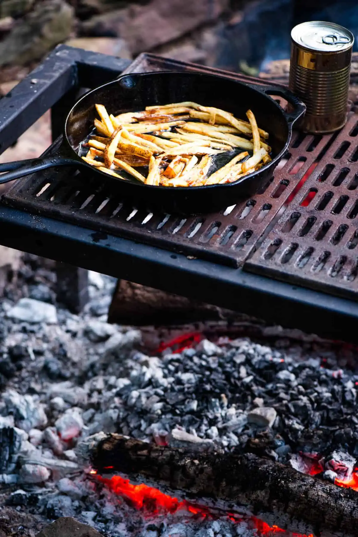 crispy French fries cooking in a cast iron skillet on a campfire grill over a bed of hot coals