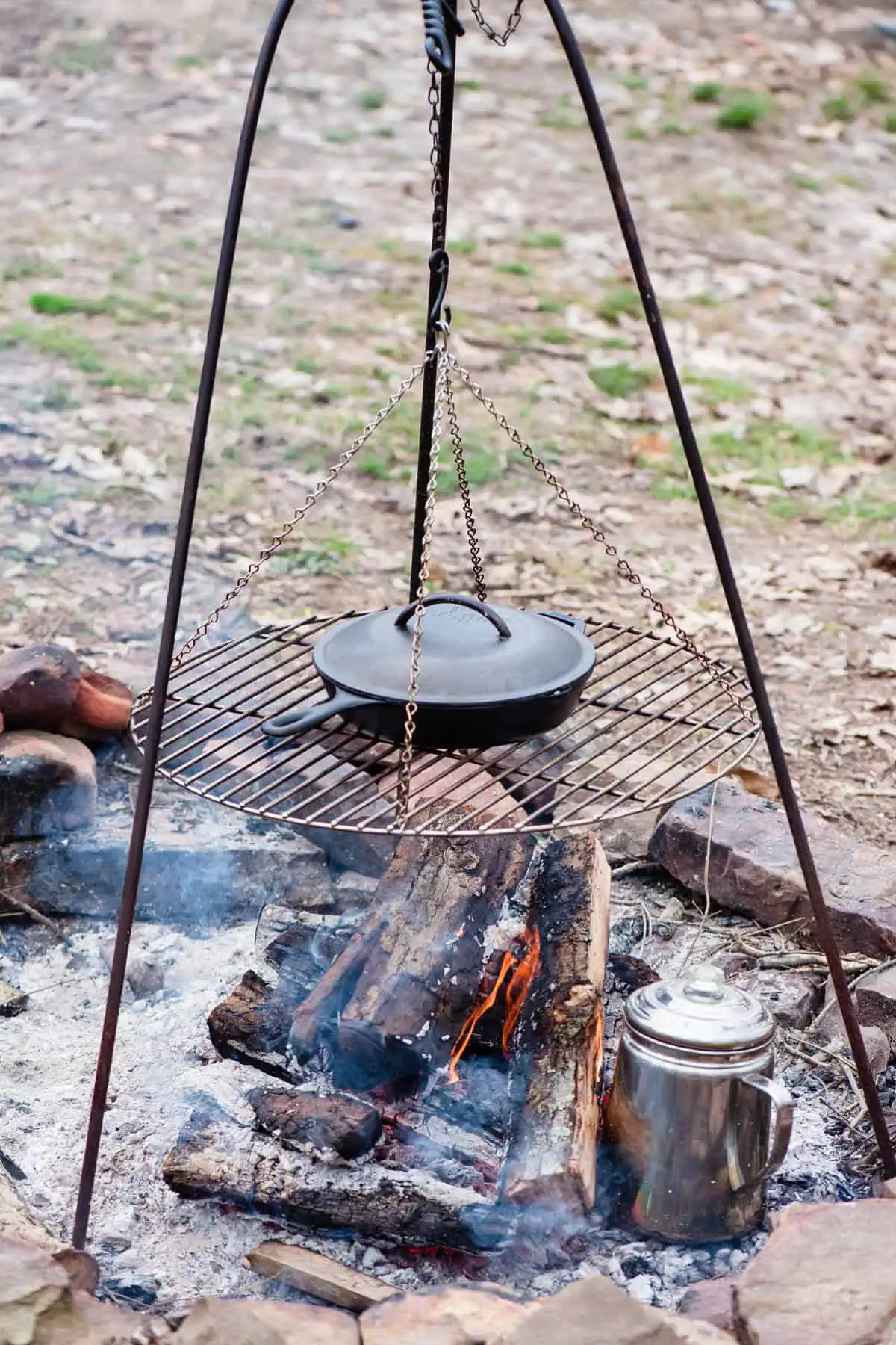 large black cast iron skillet on top of a campfire grill over a hot campfire