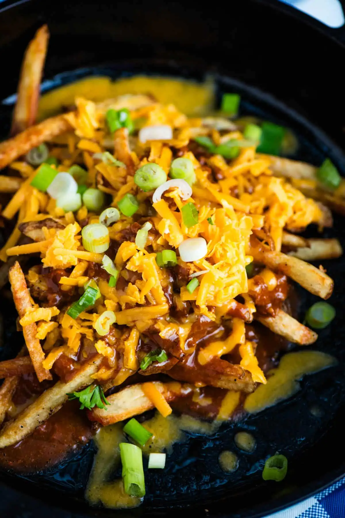 chili cheese fries with shredded cheese and green onions in a large black cast iron skillet