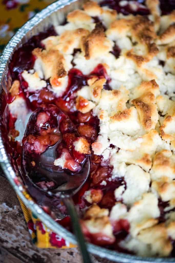 Dutch oven cobbler in an aluminum pie plate with a large silver spoon for serving