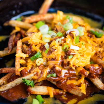 loaded chili cheese fries with shredded cheese and green onions in a large black cast iron skillet