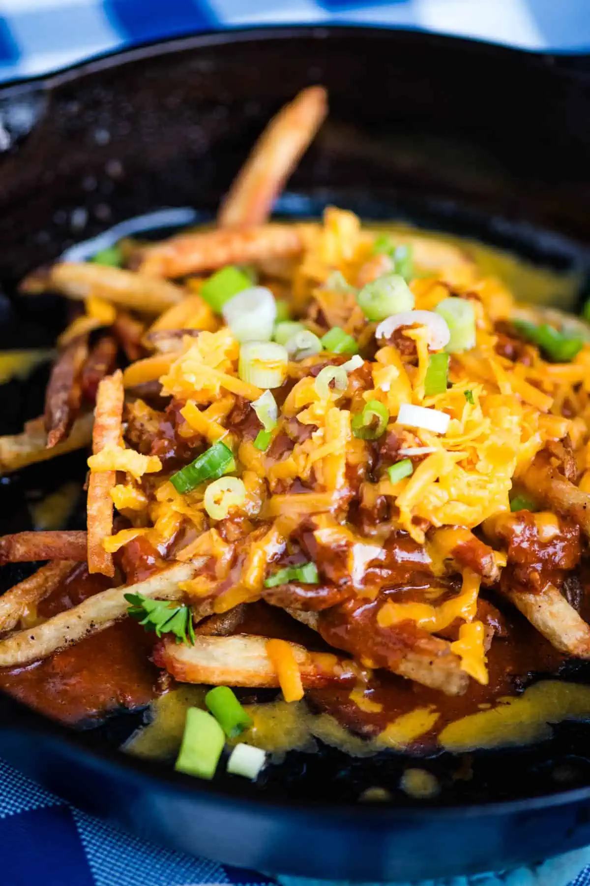 loaded chili cheese fries with shredded cheese and green onions in a large black cast iron skillet