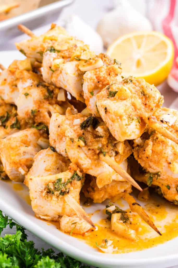 garlic parm chicken skewers stacked up in a deep dish white rectangular platter