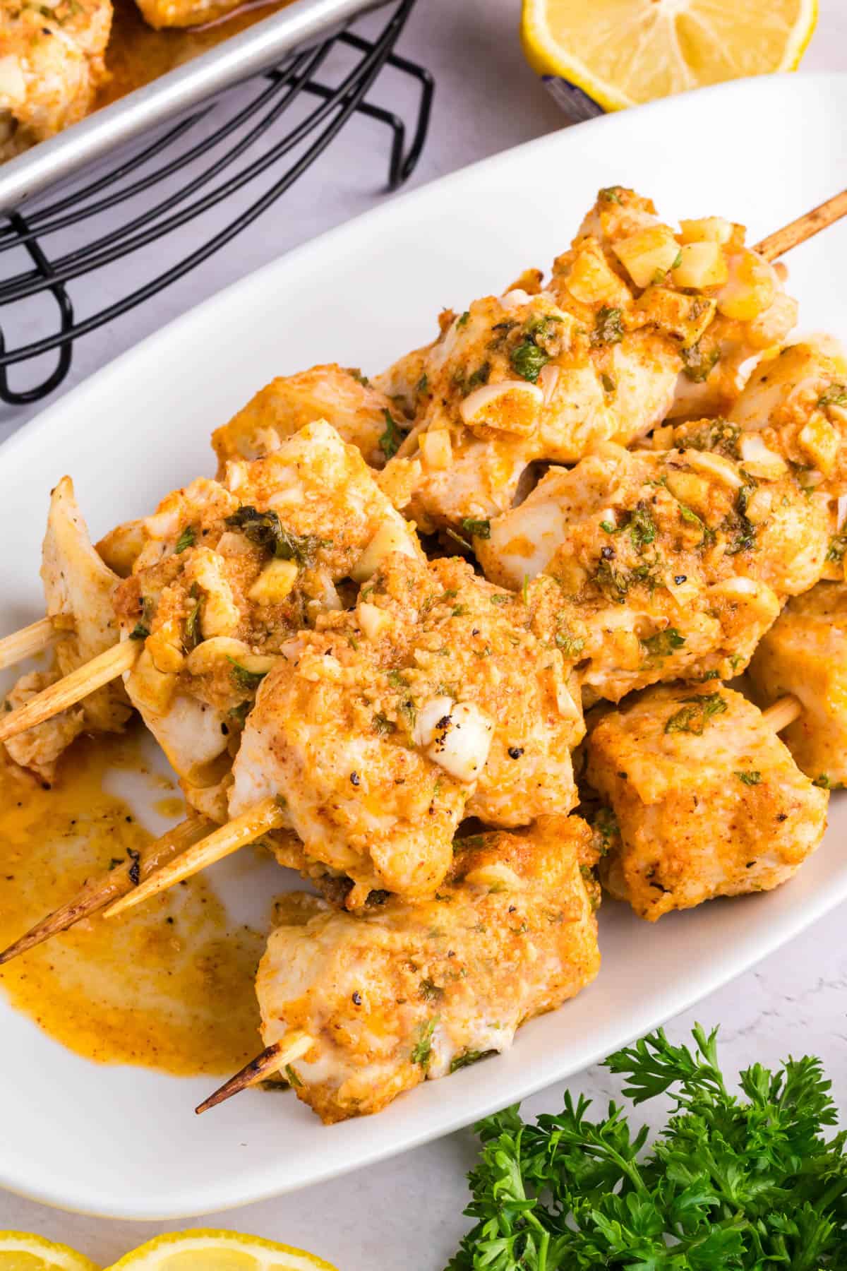 garlic parmesan chicken kabobs ready to serve on a deep dish white rectangular platter