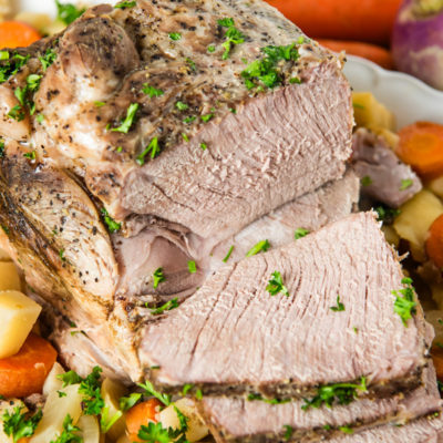 slow cooker pork roast garnished with fresh parsley on a bed of root veggies on a large white decorative plate
