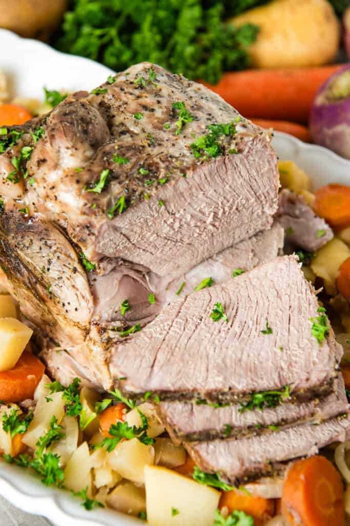 slow cooker pork roast garnished with fresh parsley on a bed of root veggies on a large white decorative plate