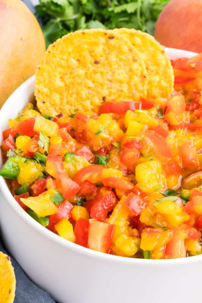 peach mango salsa in a medium white serving bowl with tortilla chips