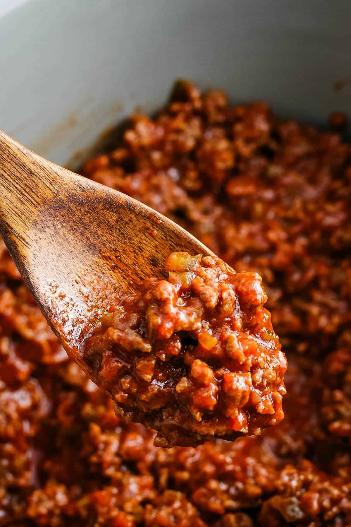 slow cooker sloppy joes on a large wooden spoon over a gray crockpot full of sloppy joes
