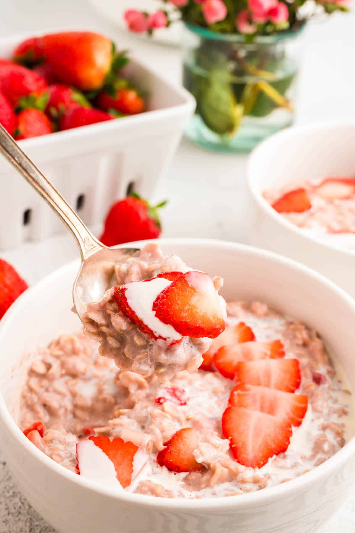 closeup photo on a heaping spoonful of strawberry oatmeal with heavy cream and sliced strawberries