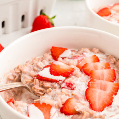 small white bowl of strawberries and cream oatmeal with heavy cream and sliced berries on top