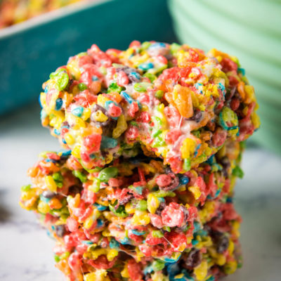 fruity pebbles treats stacked up with a bite taken out on a marbled white countertop