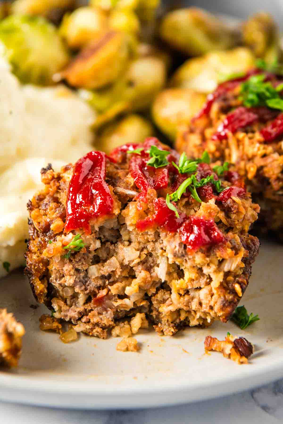 meatloaf muffins sliced in half and ready to eat on a small white plate with mashed potatoes and green beans