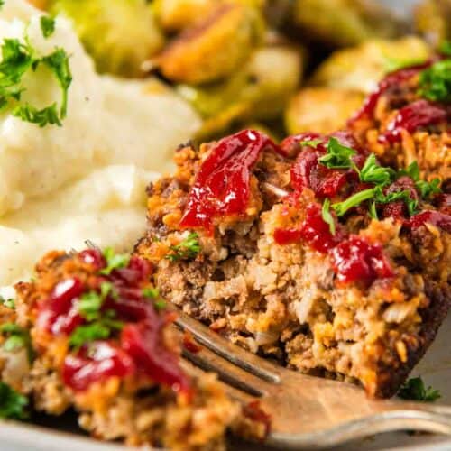 closeup photo of mini meatloaf muffins sliced in half with a silver fork on a small white plate
