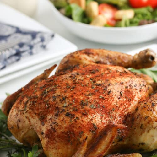 whole slow cooker chicken on a pile of fresh herbs on a large white plate next to a small bowl of fresh salad