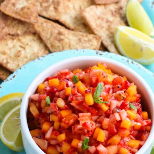 fruit salsa in a white bowl on a decorative blue saucer with fresh lemon quarters and a pile of crispy cinnamon tortilla chips