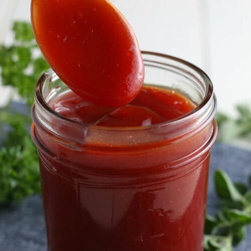 closeup photo showing spooning homemade bbq sauce into a small glass jelly jar full of homemade barbecue sauce