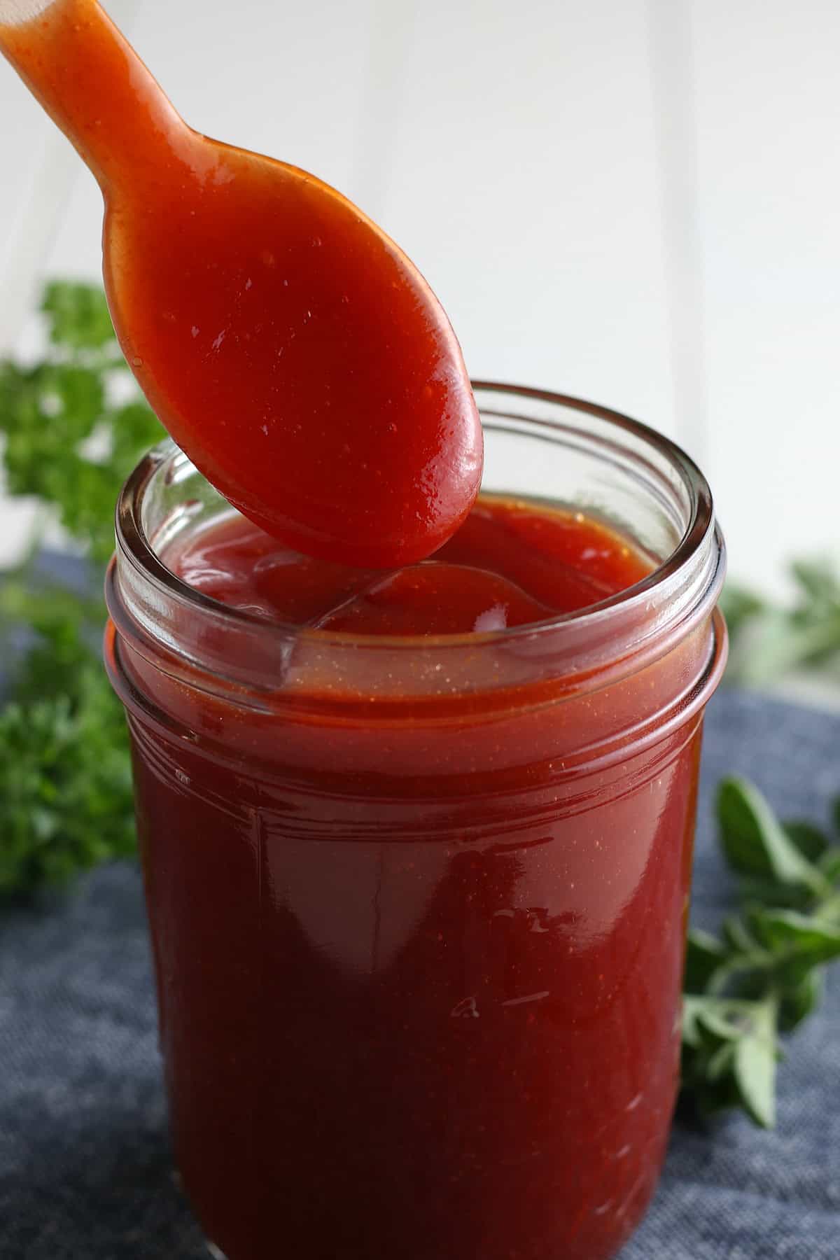 closeup photo showing spooning homemade bbq sauce into a small glass jelly jar full of homemade barbecue sauce