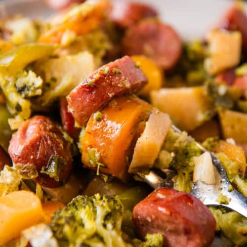 heaping forkful of juicy smoked sausage and caramelized root vegetables over a small gray plate full of sheet pan sausage and vegetables
