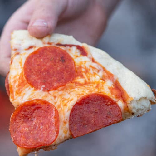 closeup photo showing hand holding up a slice of cast iron pan pizza with pepperoni
