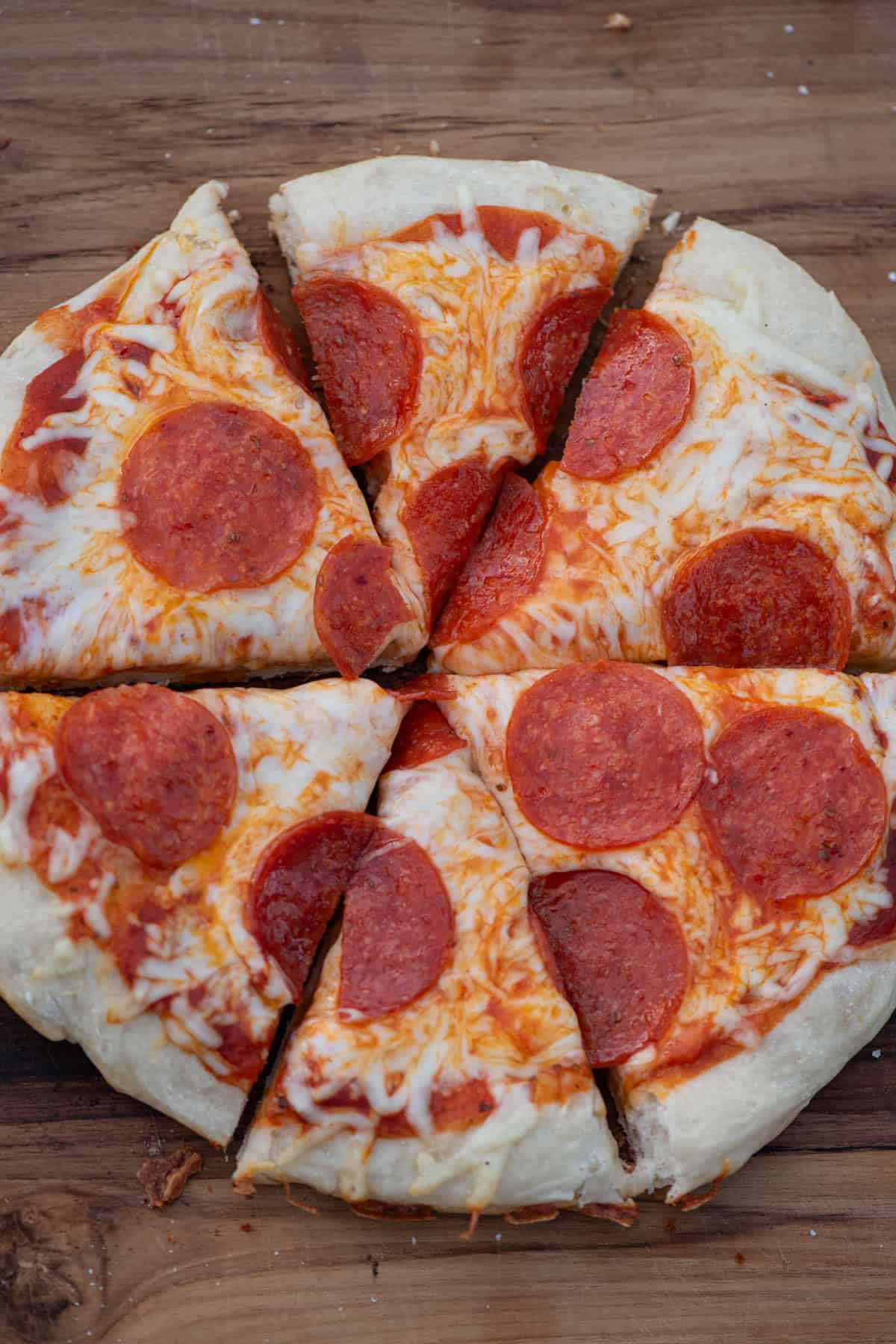 overhead shot of cast iron pizza with pepperoni on a dark brown wooden countertop