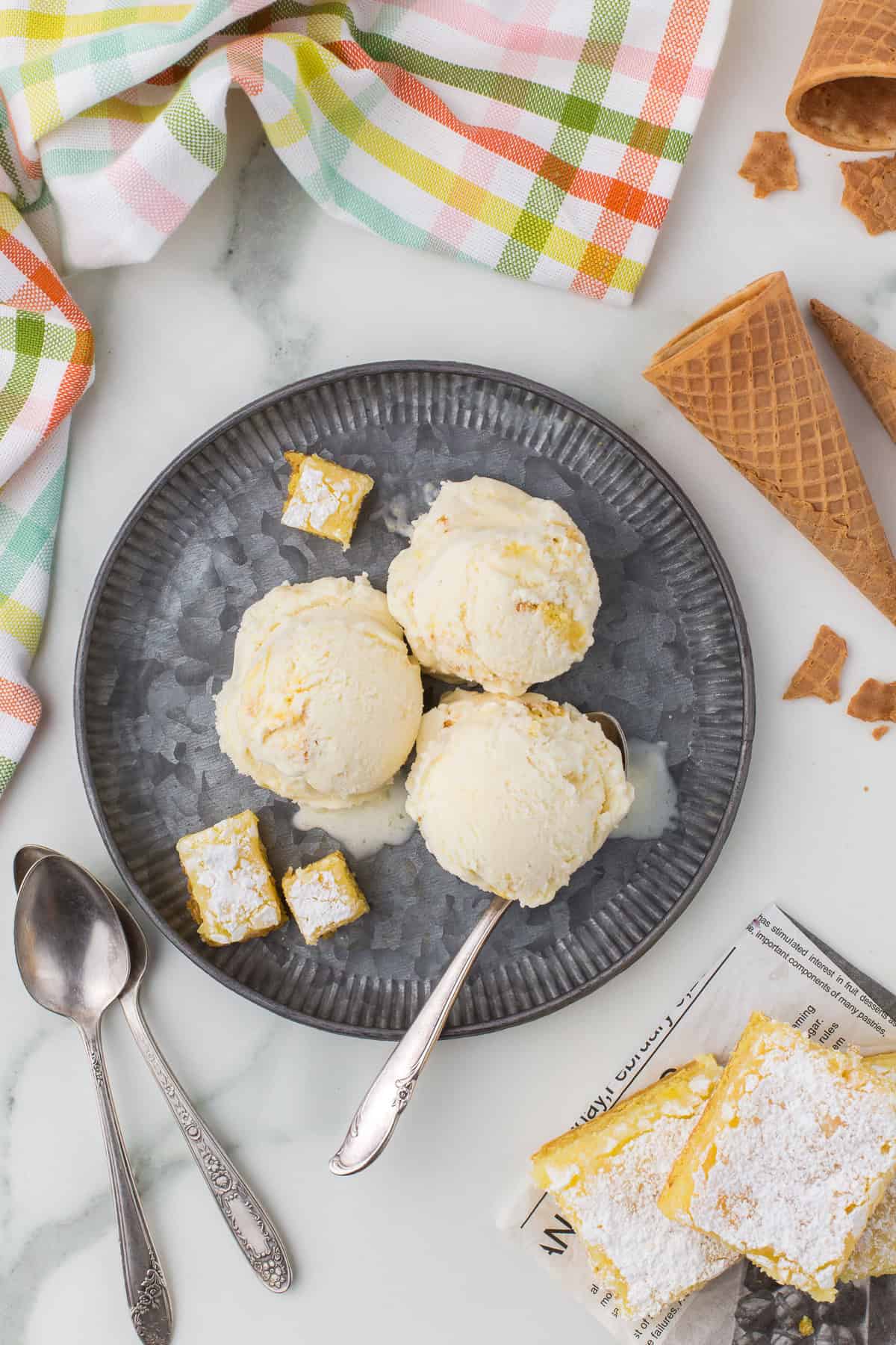 scoops of gooey butter cake frozen dessert on cold metal plate with cake pieces
