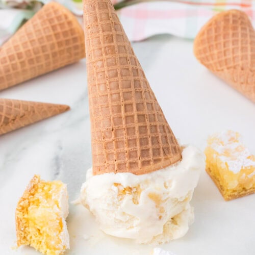 scoop of gooey butter cake ice cream on sugar cone upside down on white marble countertop