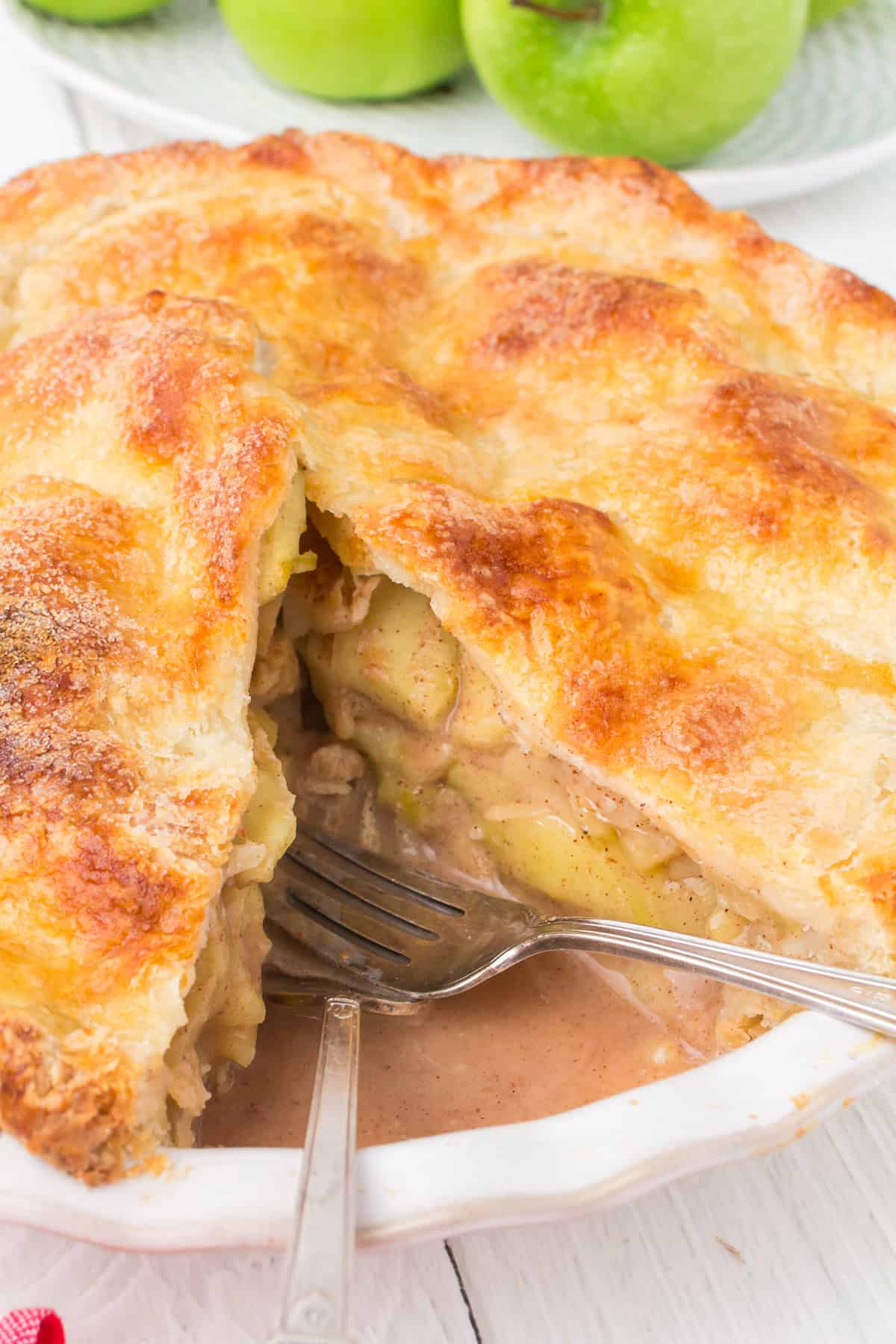 apple pie with homemade crust sliced into with serving utensils in white pie pan