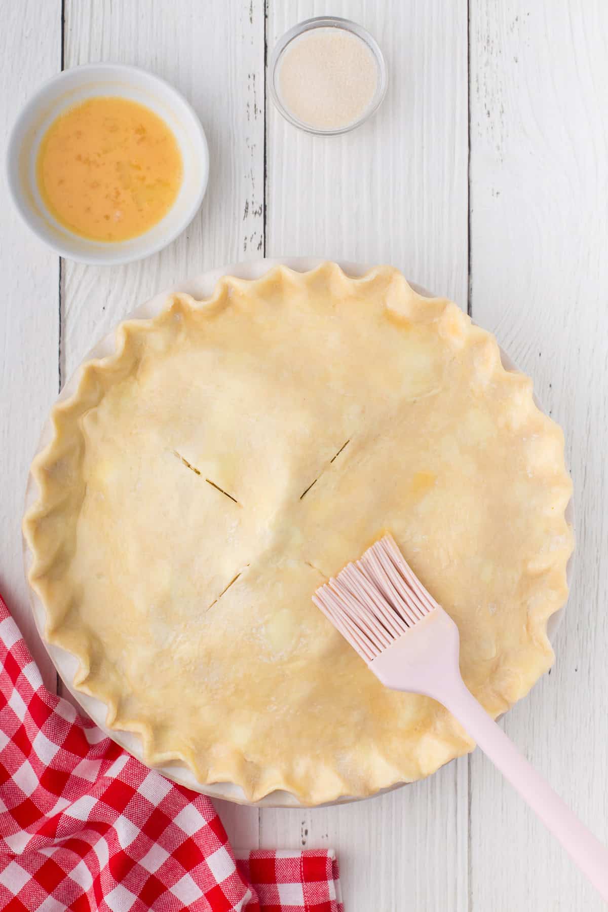 brushing egg wash on slitted pie crust apple pie