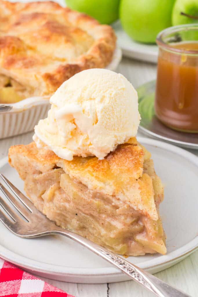 scoop vanilla ice cream on top of easy homemade apple pie slice on gray plate with fork