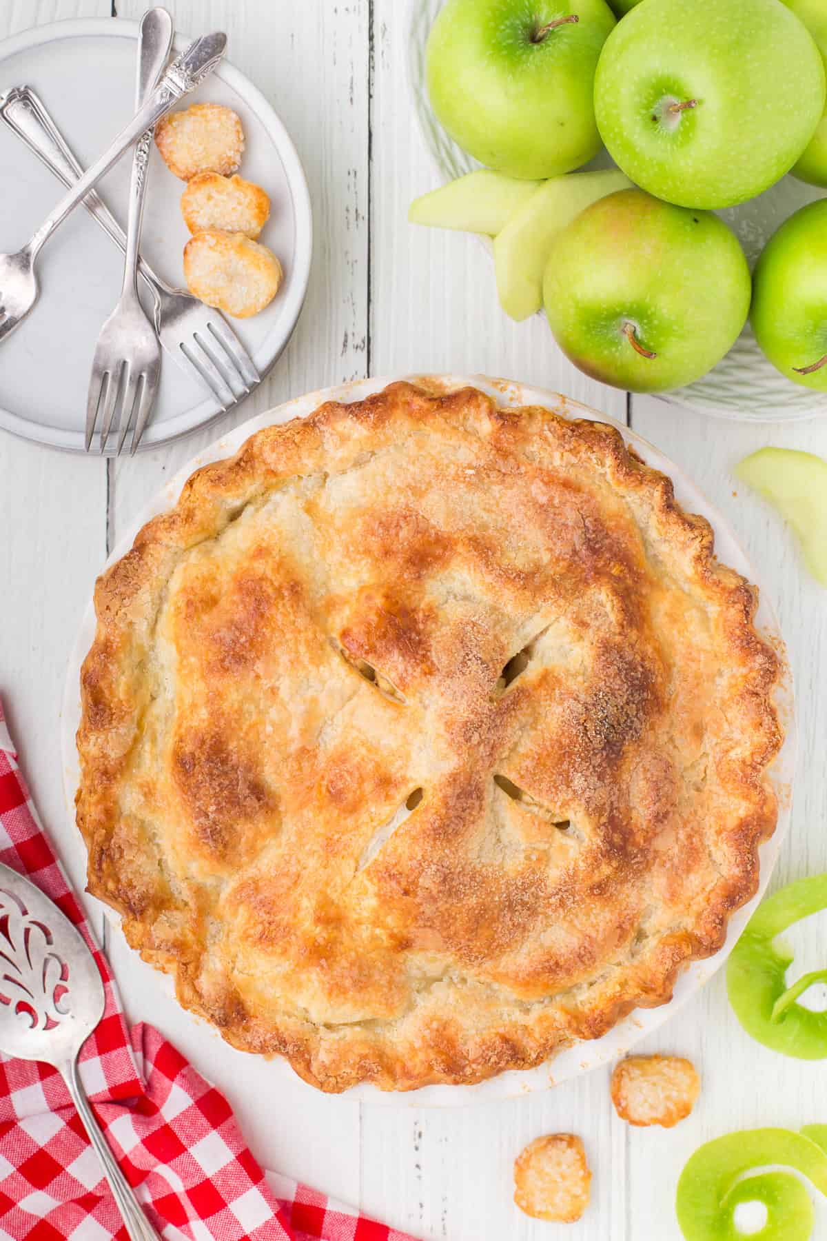 old-fashioned apple pie from scratch on white countertop with apples and plates
