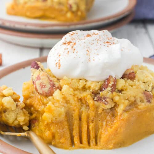 slice of pumpkin pie with cake mix on brown plate with whipped cream and fork