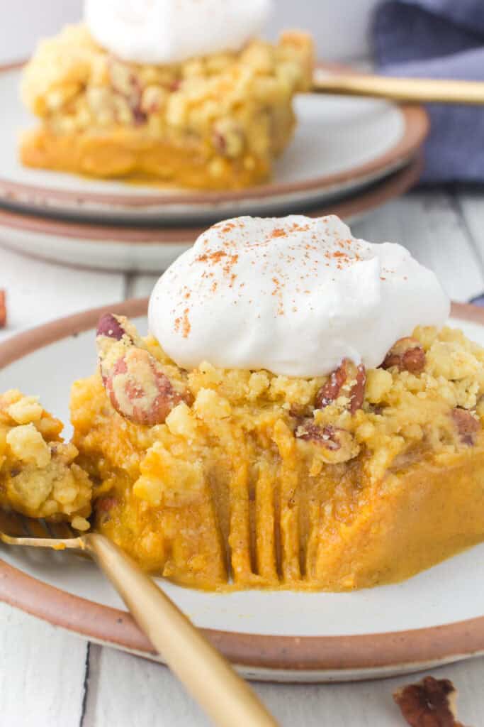 slice of pumpkin pie with cake mix on brown plate with whipped cream and fork