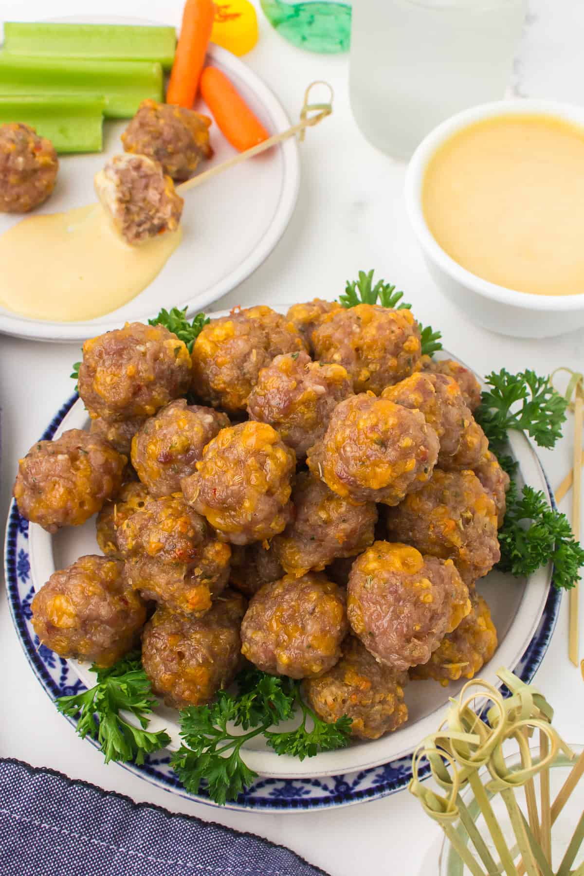 sausage and cheese balls piled up on a decorative blue and white plate with fresh parsley around the edges for garnish
