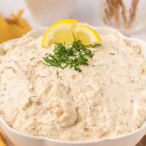 closeup photo showing white decorative bowl full of smoked salmon dip with a fresh lemon slice and fresh dill on top