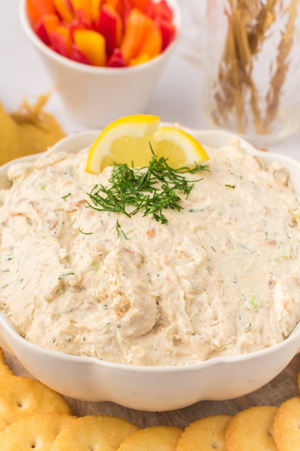closeup photo showing white decorative bowl full of smoked salmon dip with a fresh lemon slice and fresh dill on top