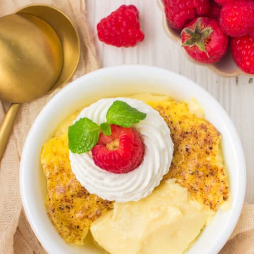 baked custard in a small white ramekin serving dish with whipped cream and fresh raspberries on top