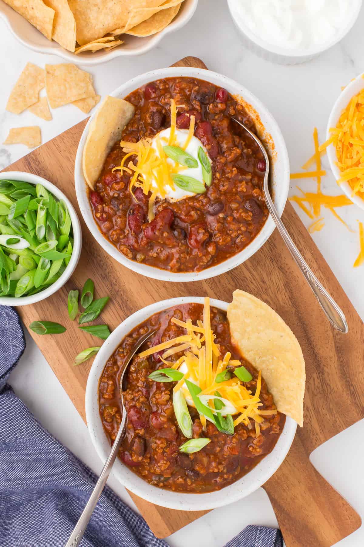 2 bowls full of homemade chili con carne on a small wooden cutting board
