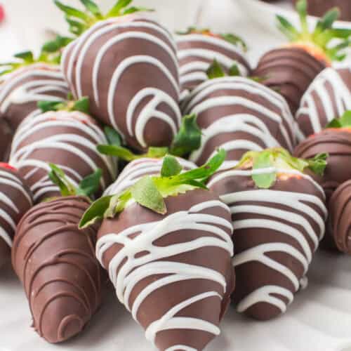 assortment of chocolate covered strawberries with a white chocolate drizzle on a decorative white plate