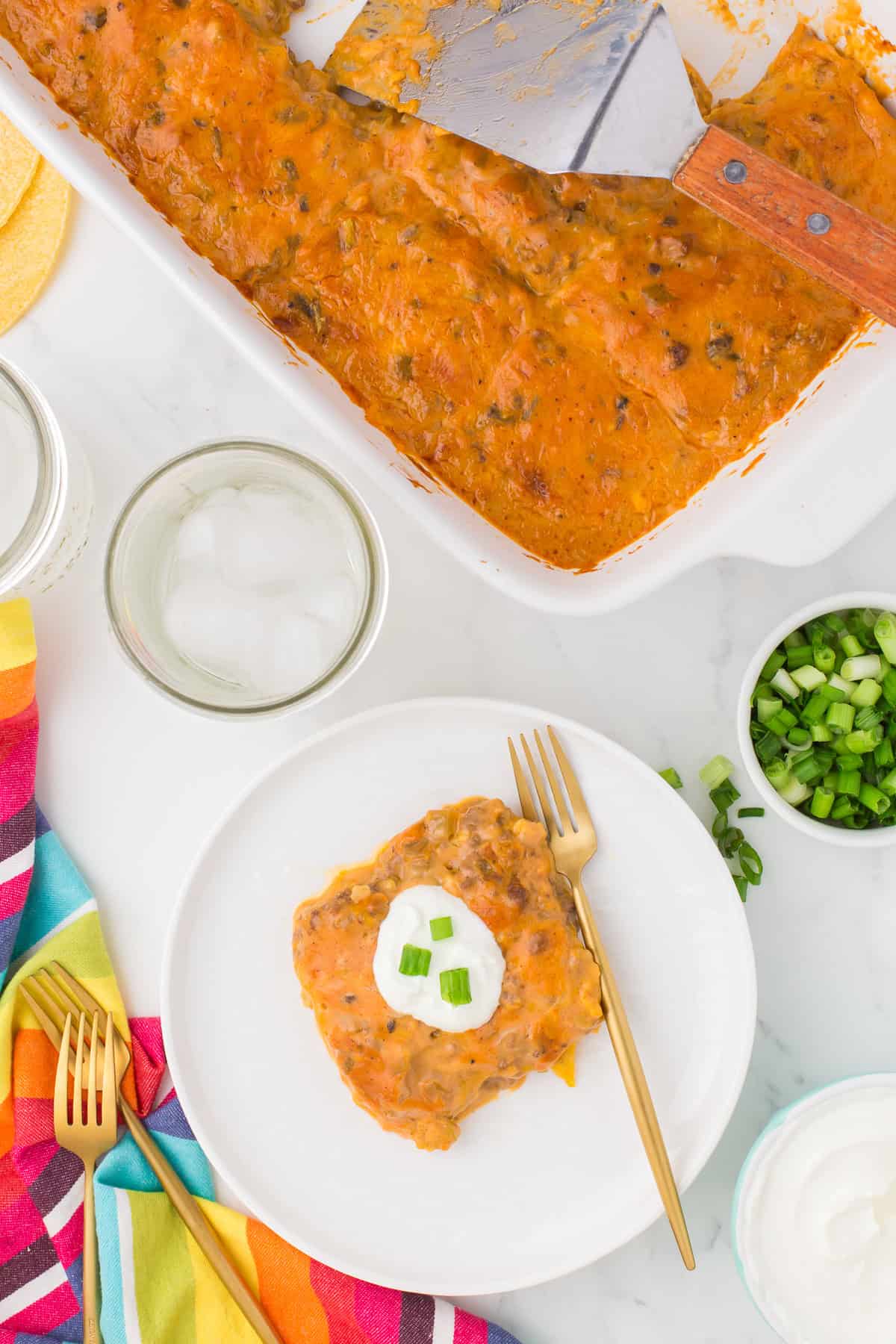 overhead photo of ground beef enchilada casserole on a small white plate with sour cream and green onions on top