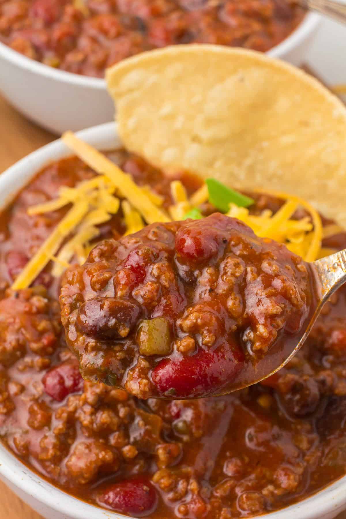 spoonful of chili con carne over a small white bowl full of chili con carne with a tortilla chip