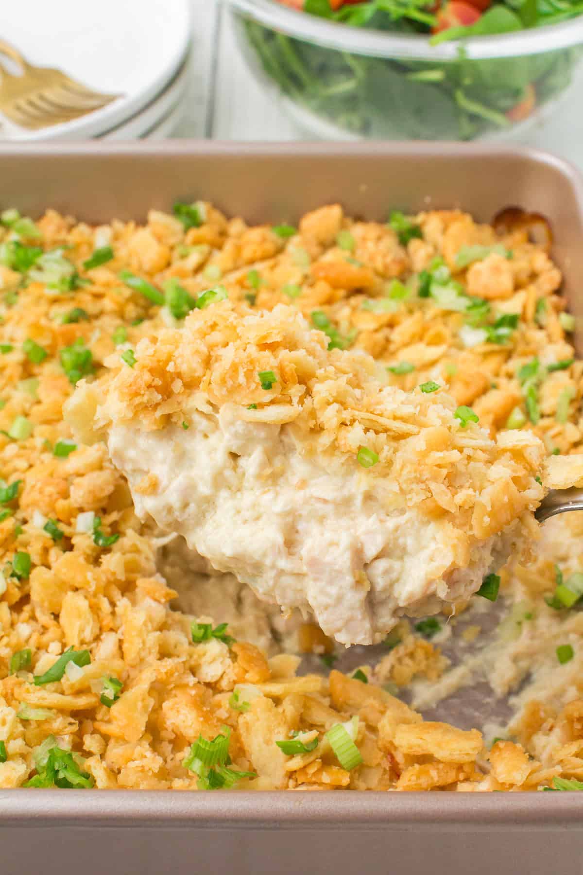 scoop of chicken casserole with Ritz crackers on top over a large square pan full of Ritz cracker chicken casserole