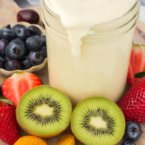 creamy fruit salad dressing in a small glass jar on a wooden cutting board with fresh fruit