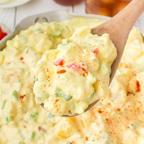 closeup photo showing a large wooden spoonful of deviled egg potato salad