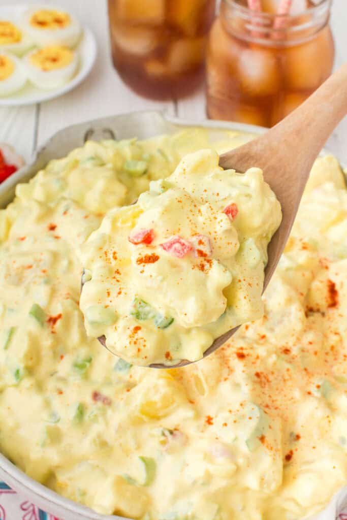 closeup photo showing a large wooden spoonful of deviled egg potato salad