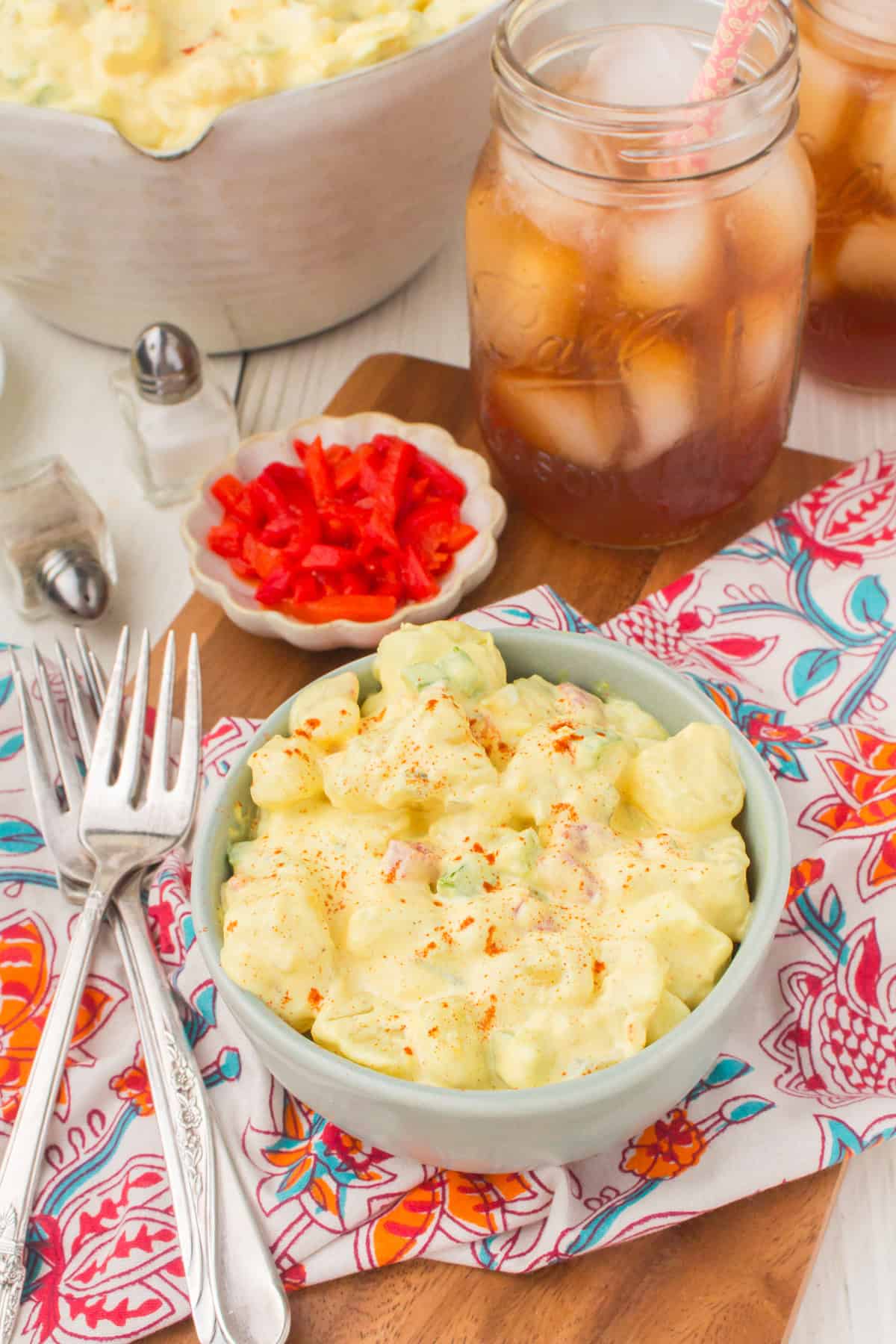 deviled egg potato salad in a small gray bowl with 2 forks and a small glass of iced tea on the side