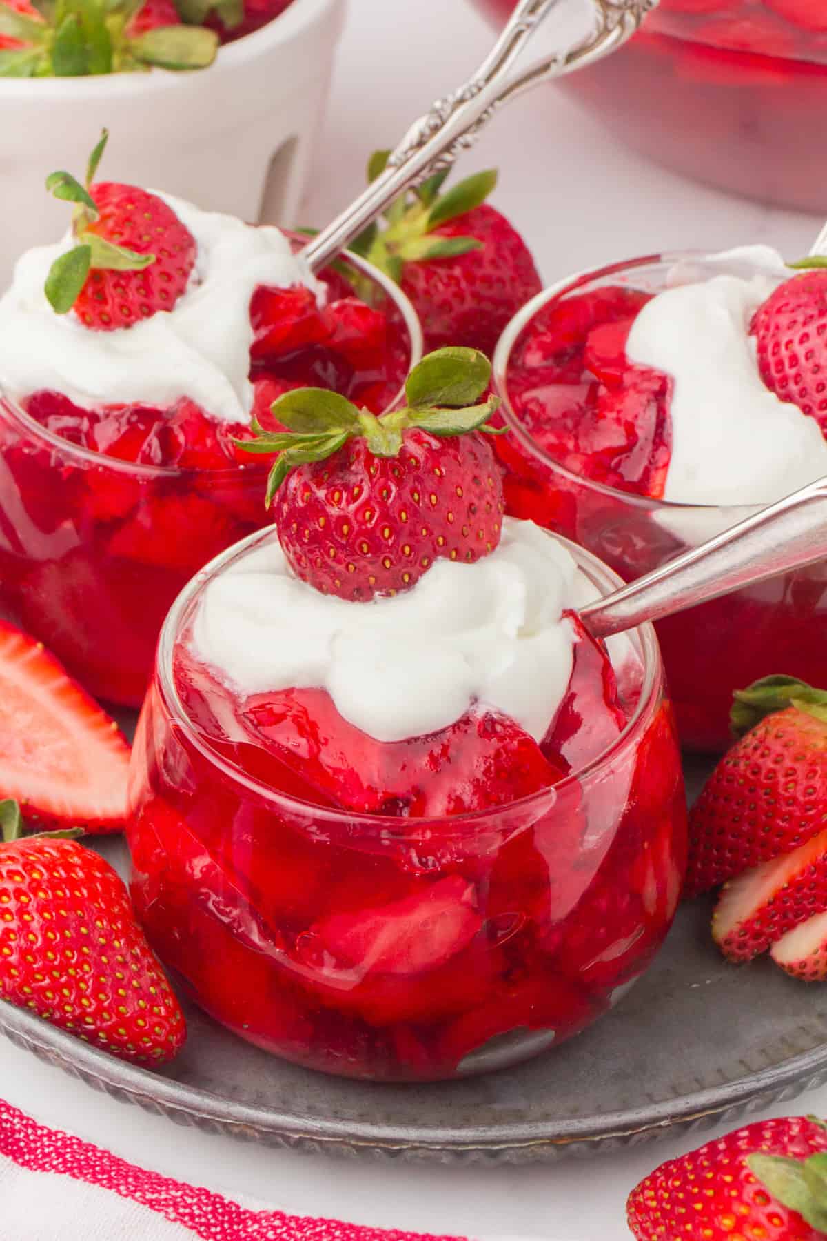 strawberry Jello with real strawberries in a small glass dish with whipped cream and fresh fruit on top