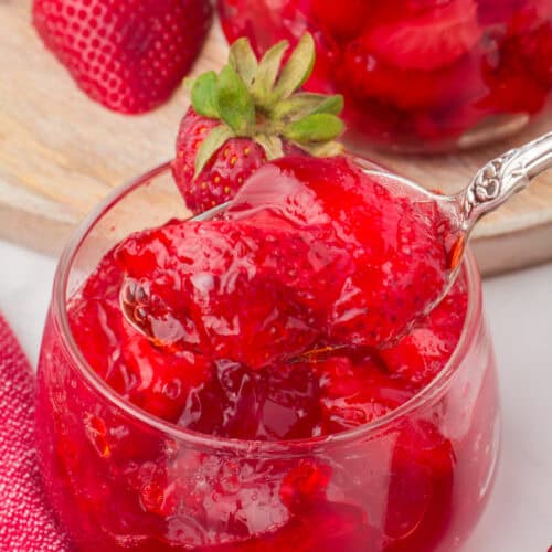 spoonful of strawberry Jello with frozen strawberries in a small glass dish