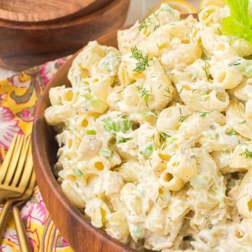 tuna macaroni salad served in a large brown wooden bowl with a sprig of celery leaf on top for garnish